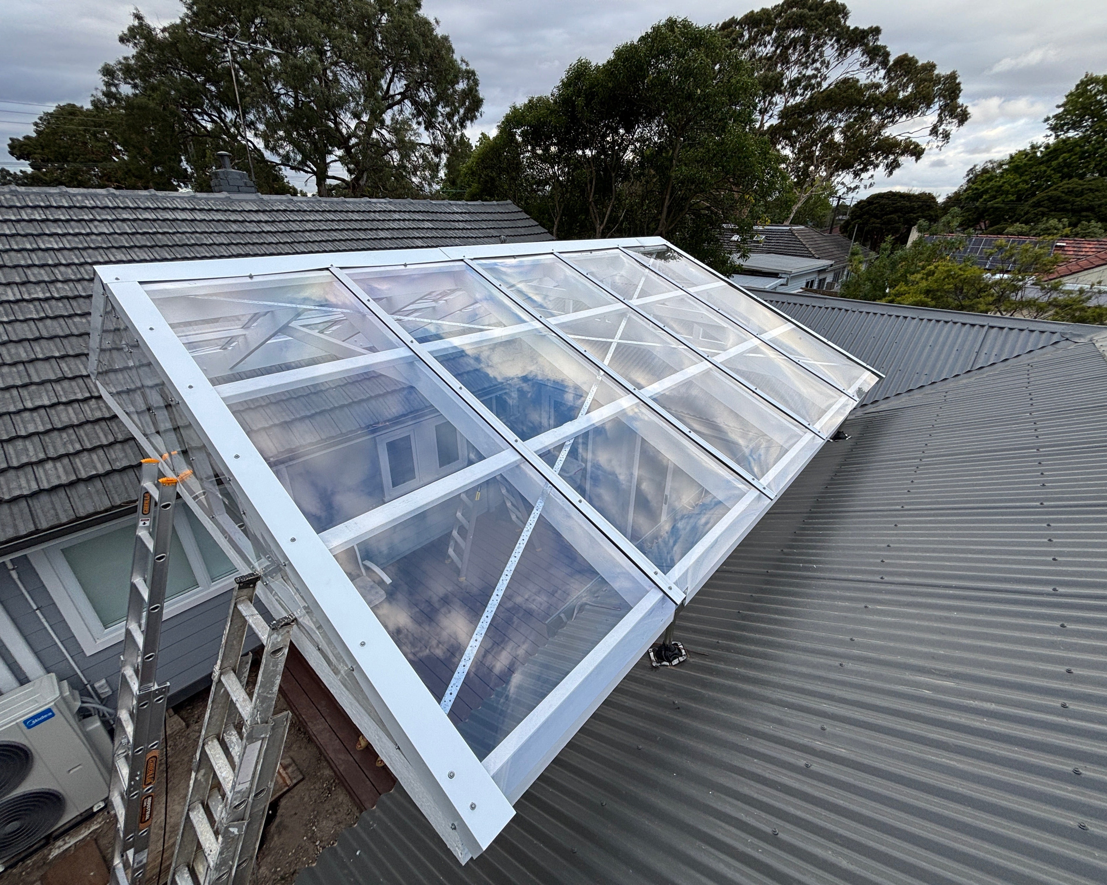 A glass conservatory extension with a white timber frame and clear glass-like Polycarbonate roof panels